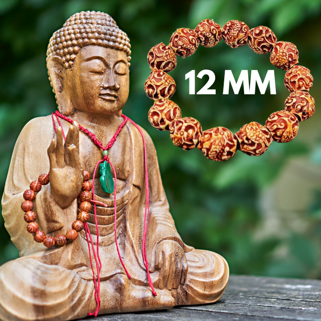 A wooden Buddha statue with prayer beads and a jade pendant sits outdoors. Next to it, a Phoenix Bird Meditation Bracelet by Snazzy Jahzzie with intricate designs is labeled "12 MM." The background features blurred green foliage.