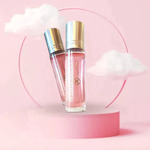 Two pink and gold perfume bottles stand on a pink circular platform with fluffy white clouds in the background, set against a pastel pink backdrop. The elegance of Snazzy Jahzzie® Phero Perfume bottles by Snazzy Jahzzie LLC and the dreamlike background create a sense of charm and femininity.